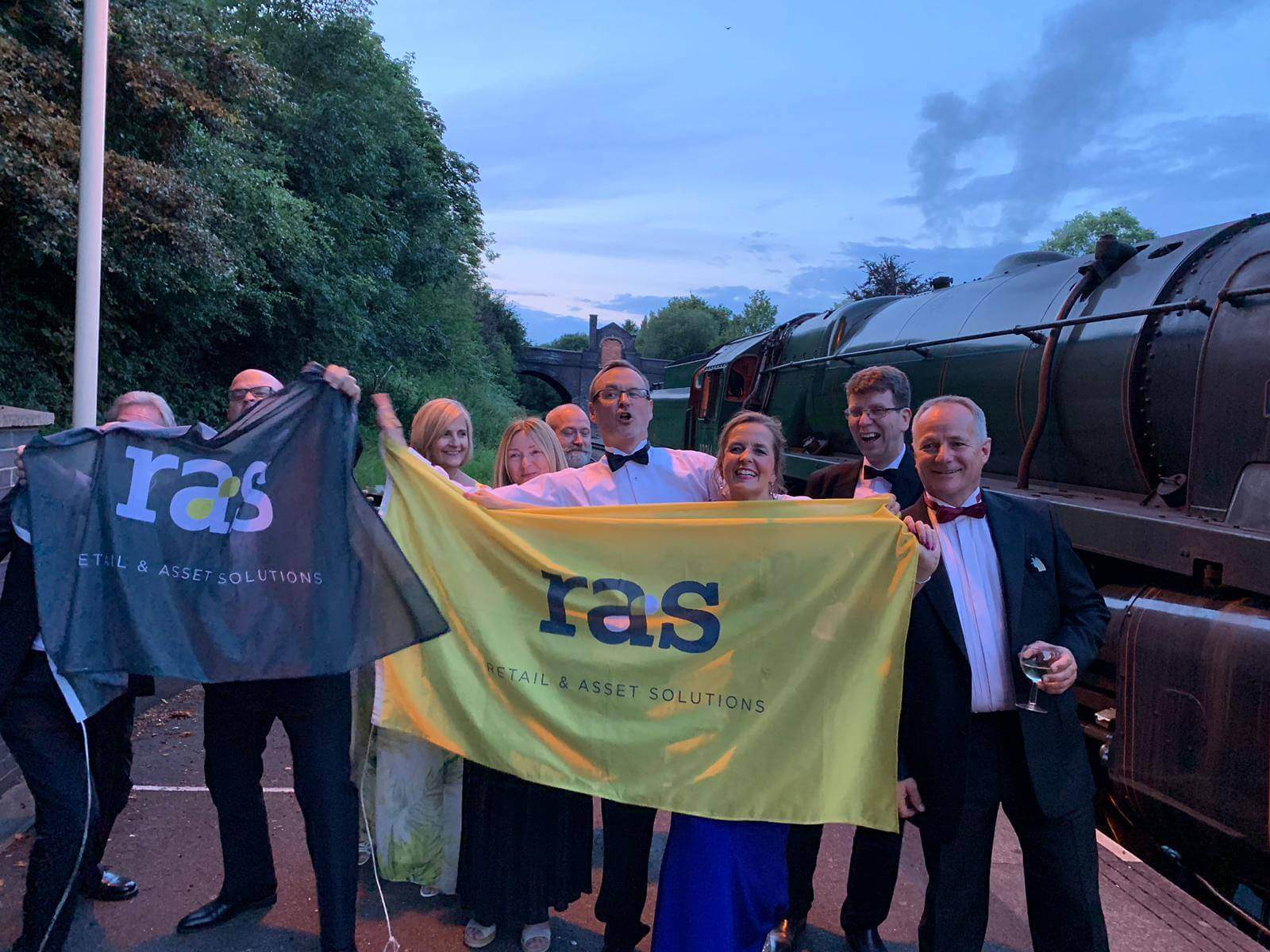 RAS employees holding RAS branded flags on a train platform.